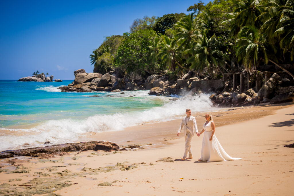 Brautpaar spaziert Hand in Hand am Strand mit Palmen und Granitfelsen – Hochzeitsfotos Seychellen